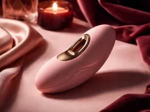 Розовый вибратор на мягкой ткани при тёплом свечном свете